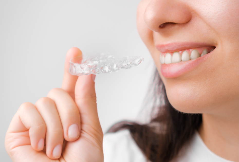 A woman smiling while holding a clear dental aligner near her teeth, representing invisible aligners for teeth straightening in the UK.