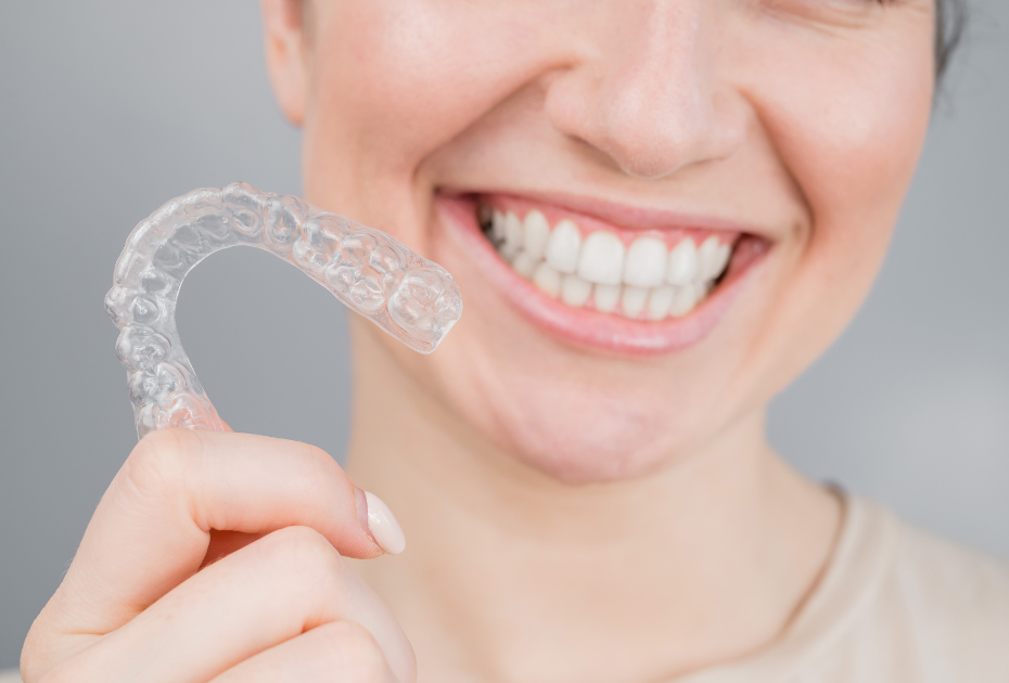 Person smiling while holding clear aligners, showcasing a discreet teeth straightening option for smile correction in the UK.