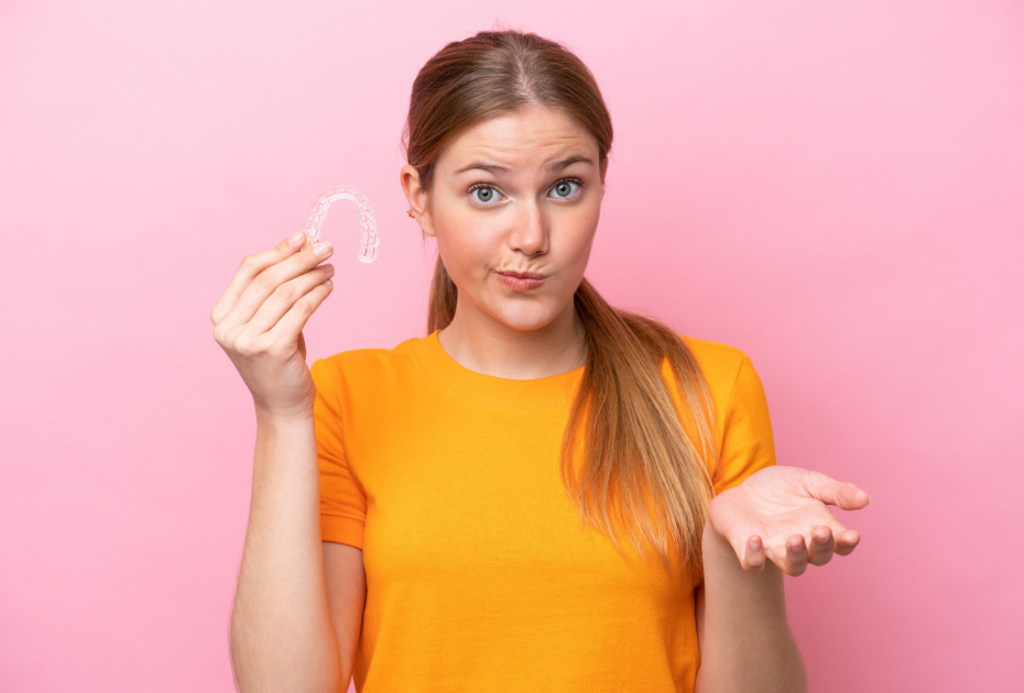Woman holding invisible aligners looking unsure, representing what clear aligners are and how they work.