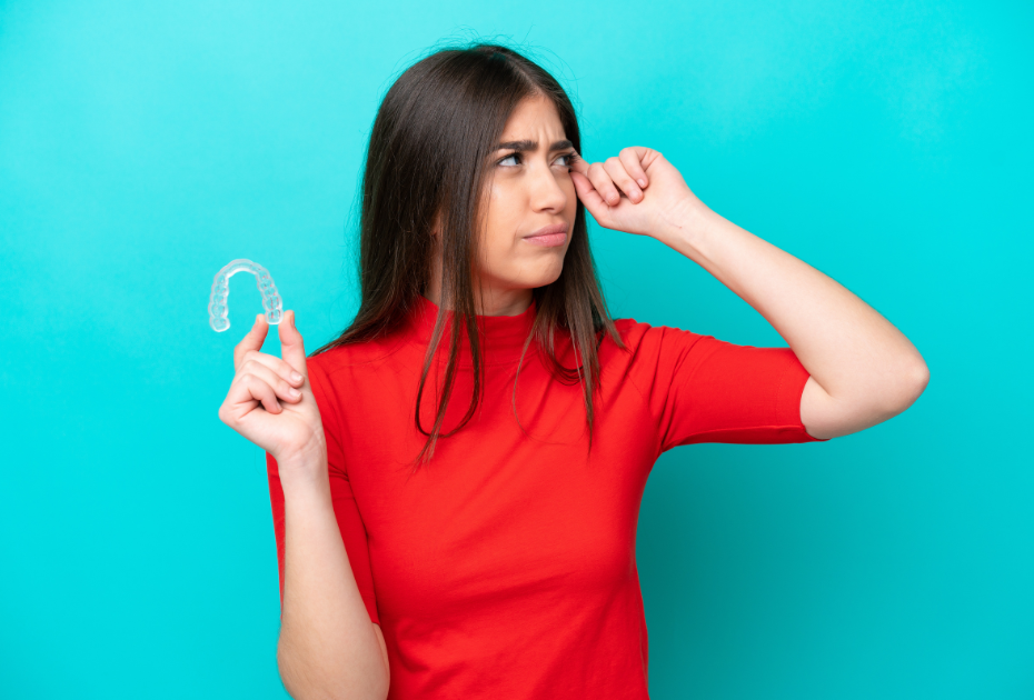 Confused woman holding clear aligner tray, considering teeth straightening suitability for clear aligners in the UK.