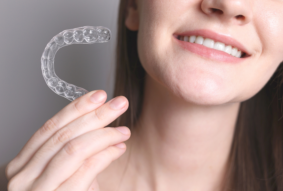 Woman smiling and holding a clear dental retainer